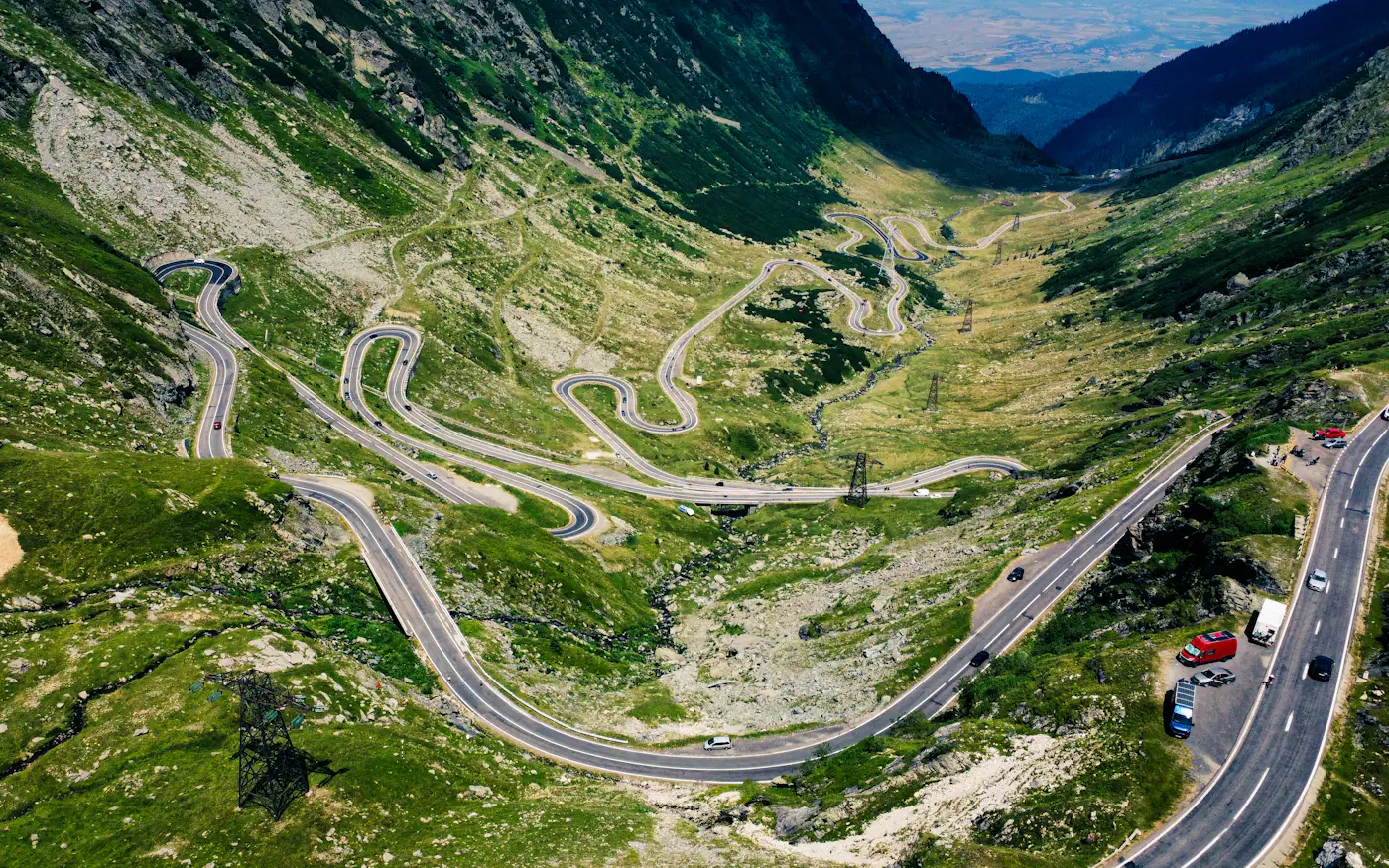 A mountain road switching back and forth up a green valley, from above