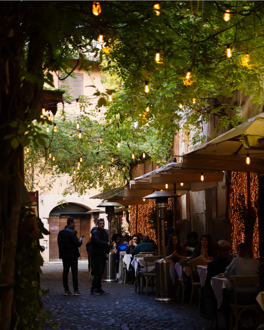 Diners at tables under string lights in an old town street