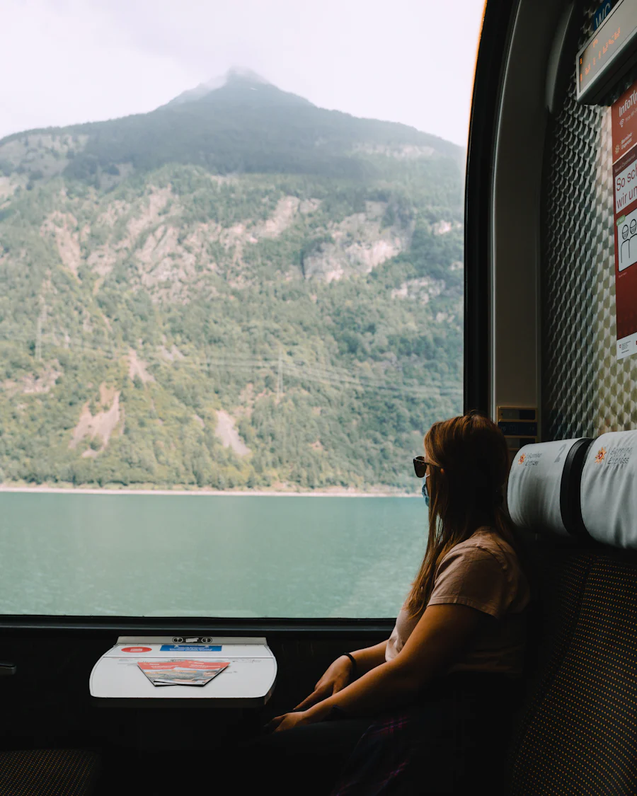 A traveller at a train window, watching a lake and mountains go by