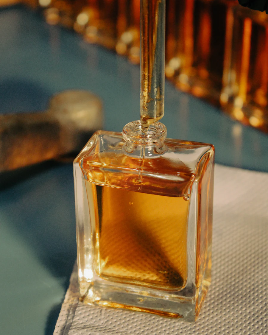 A glass pipette drawing amber perfume from a square bottle