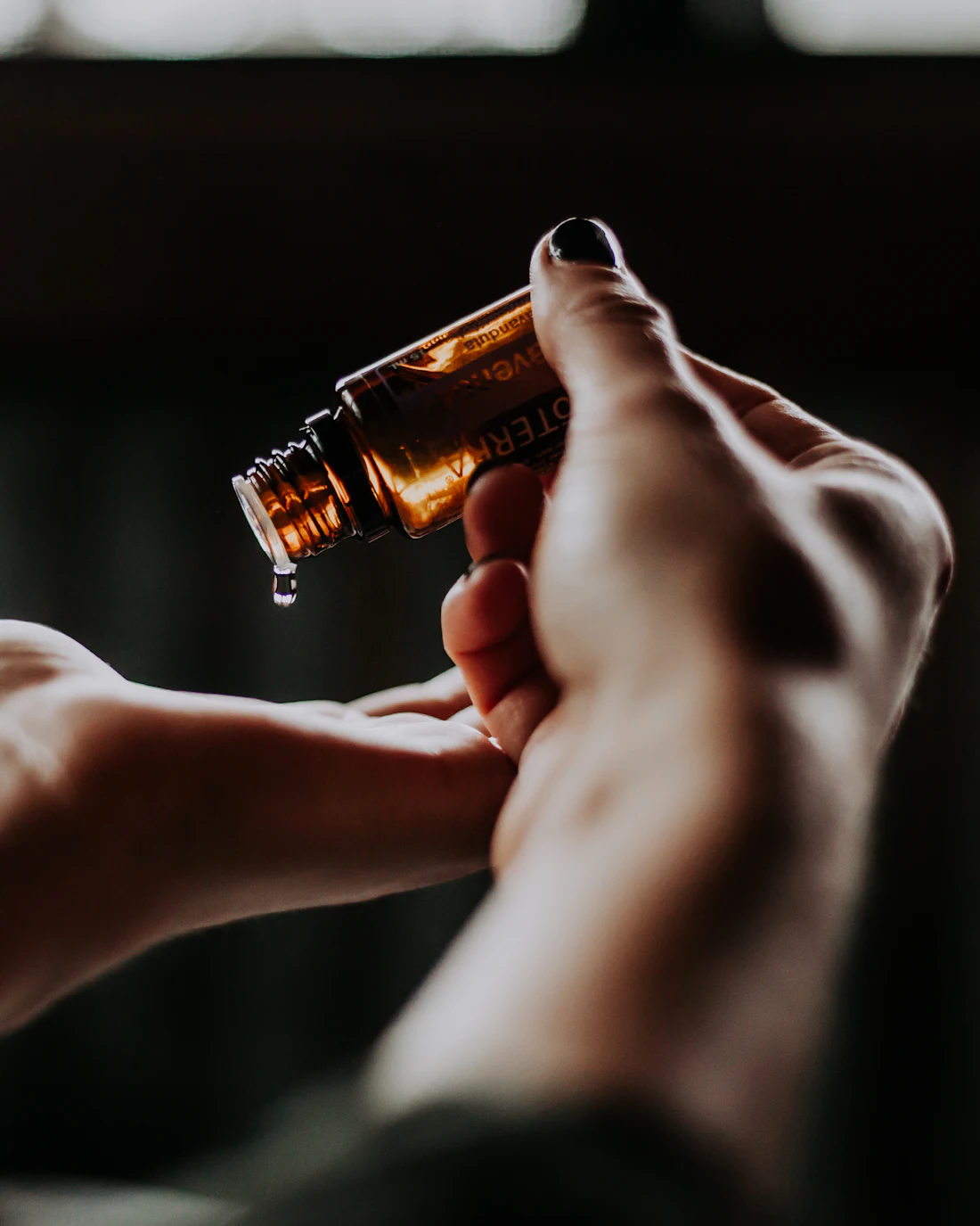 A drop of perfume oil falling from an amber vial onto a wrist